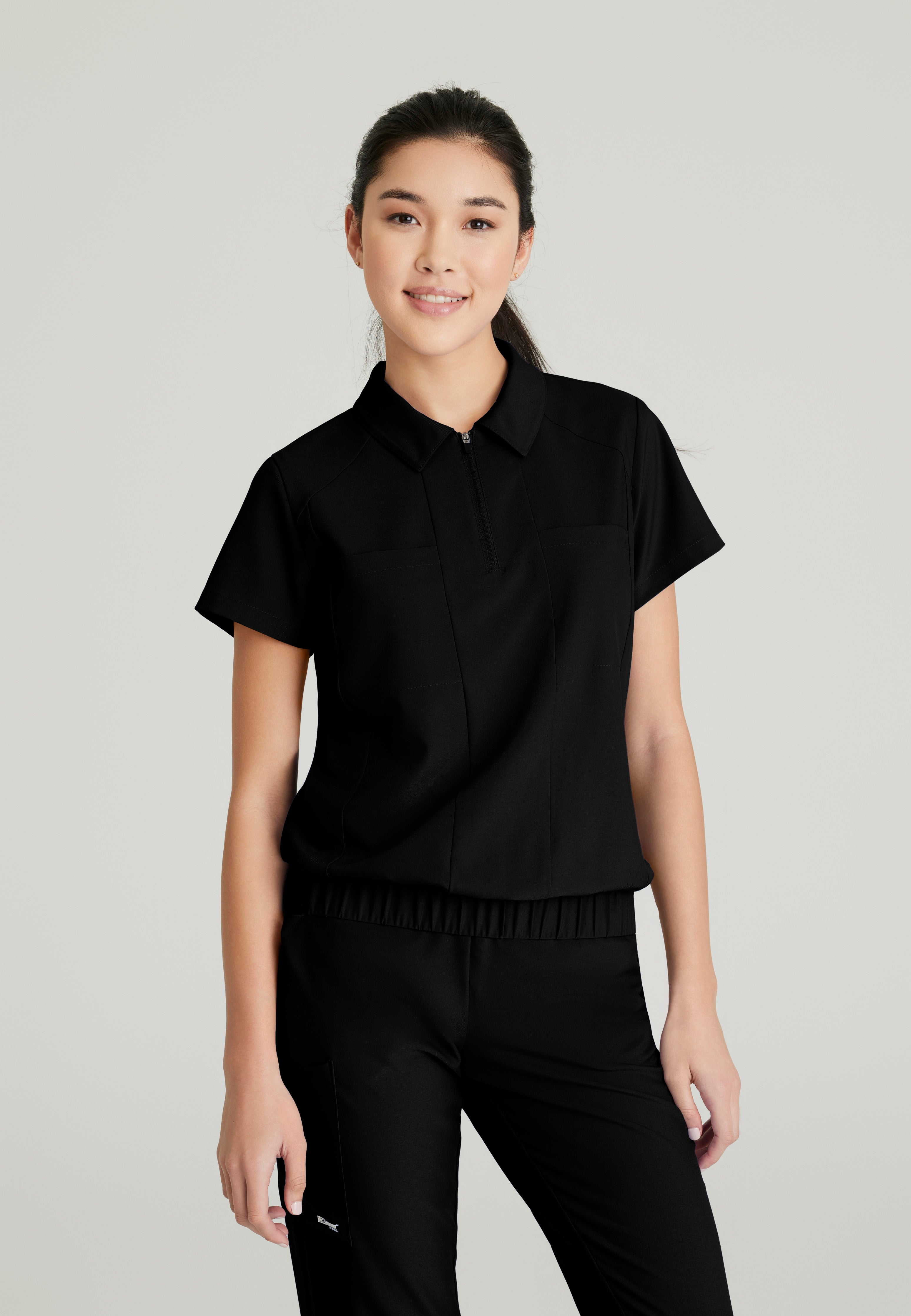 Front View of the Perseverance 2-Pocket Zip Neck Banded Waist Top in Black from Grey's Anatomy™ by Barco Evolve