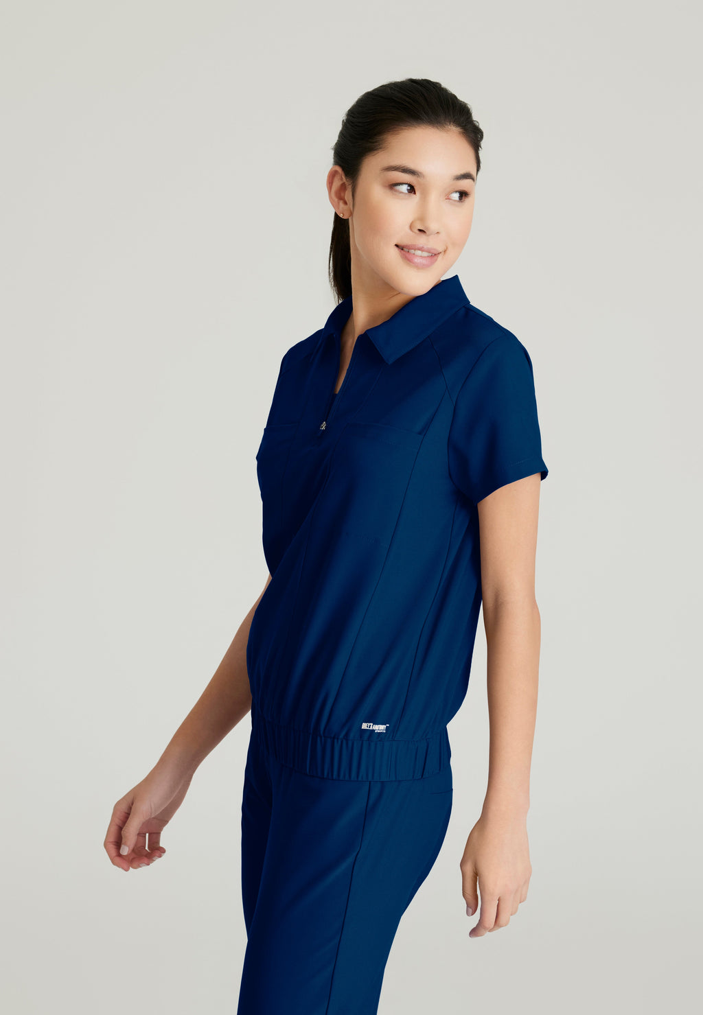 Side View of the Perseverance 2-Pocket Zip Neck Banded Waist Top in Indigo from Grey's Anatomy™ by Barco Evolve
