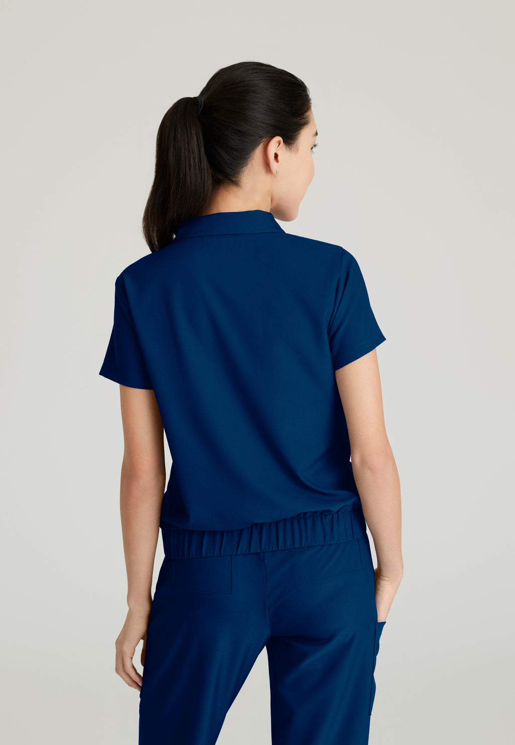 Back View of the Perseverance 2-Pocket Zip Neck Banded Waist Top in Indigo from Grey's Anatomy™ by Barco Evolve