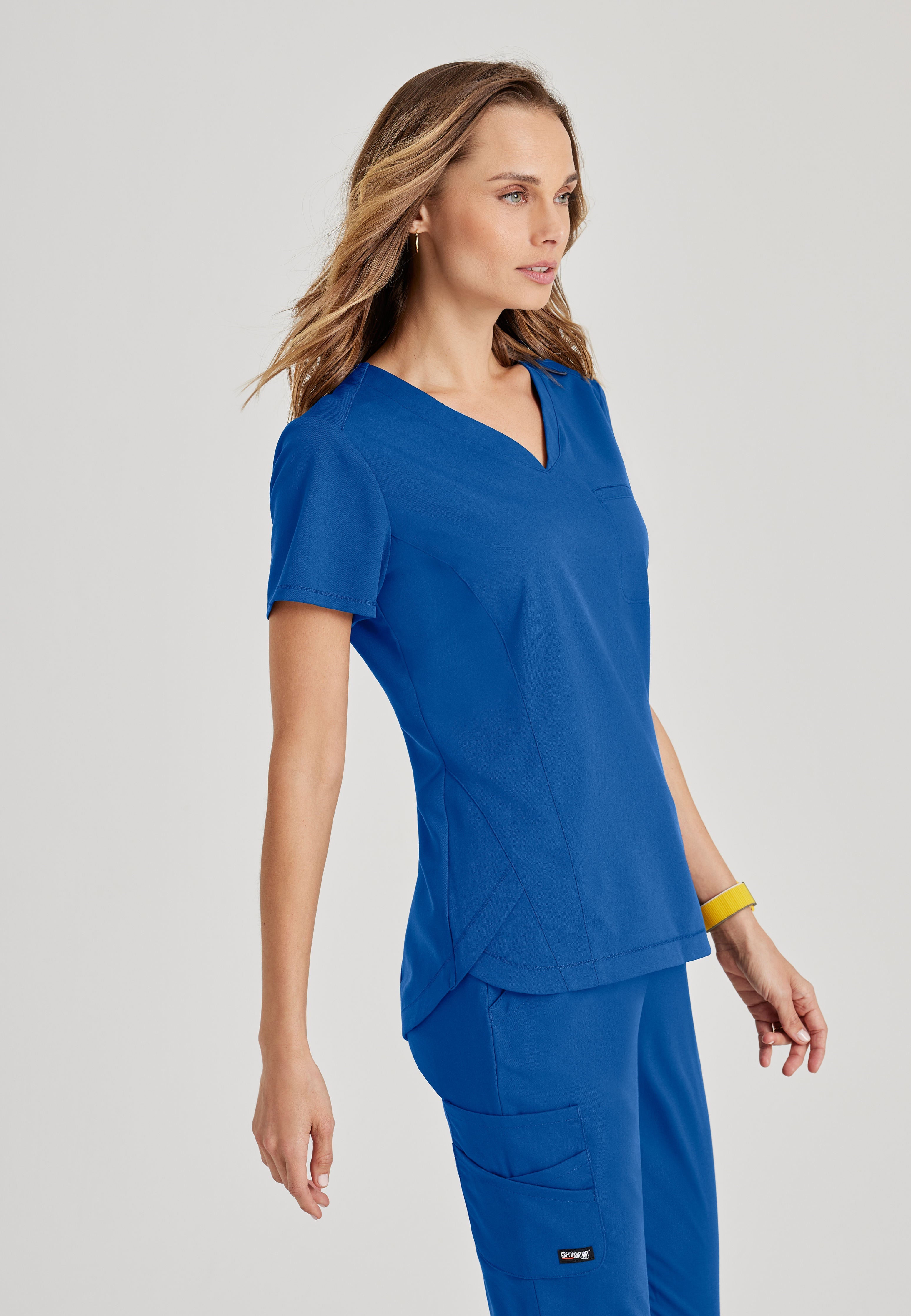 Side View of the Capri 2-Pocket Hourglass V-Neck Scrub Top in New Royal from Grey's Anatomy™ by Barco Spandex Stretch