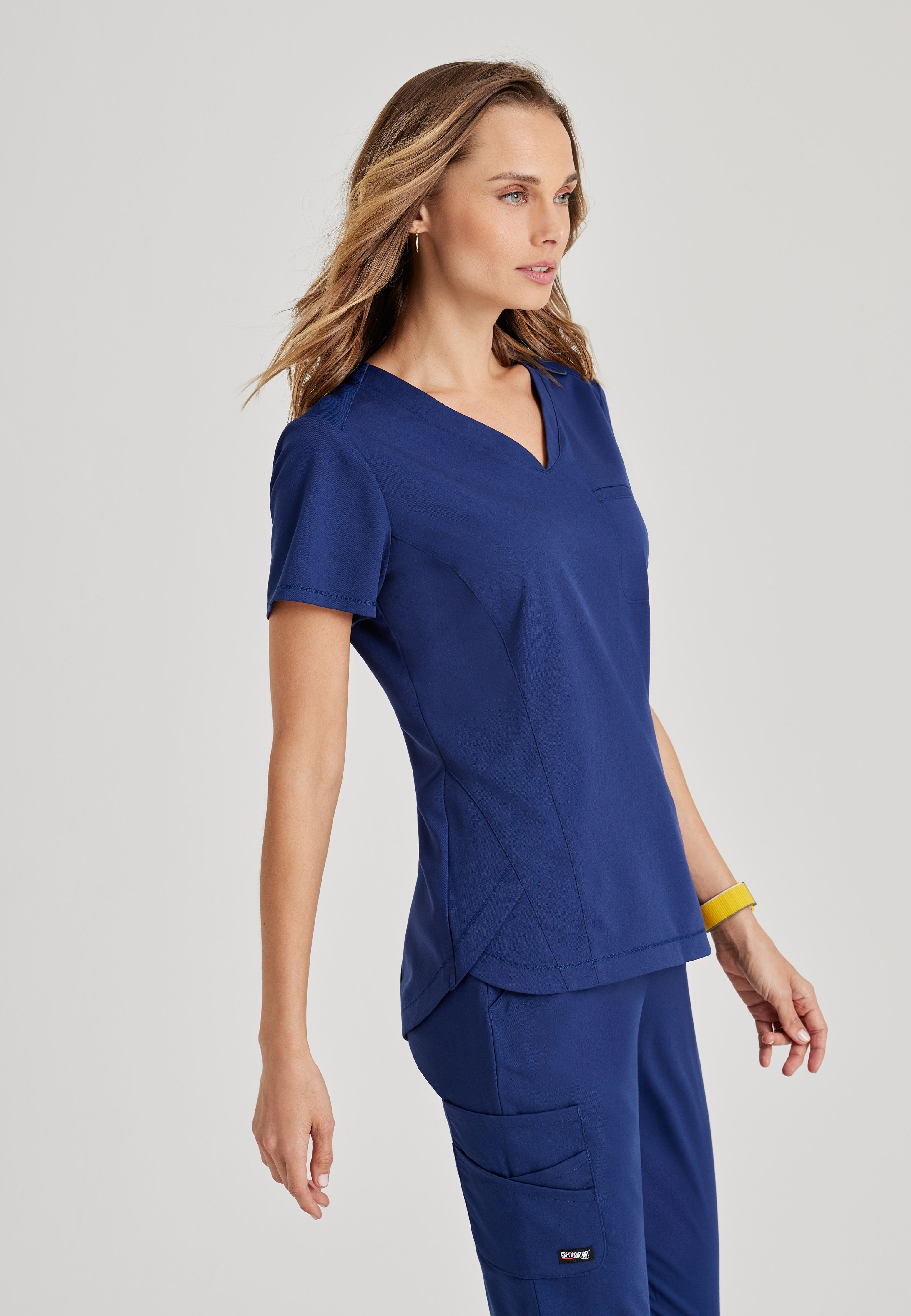 Side View of the Capri 2-Pocket Hourglass V-Neck Scrub Top in Indigo from Grey's Anatomy™ by Barco Spandex Stretch