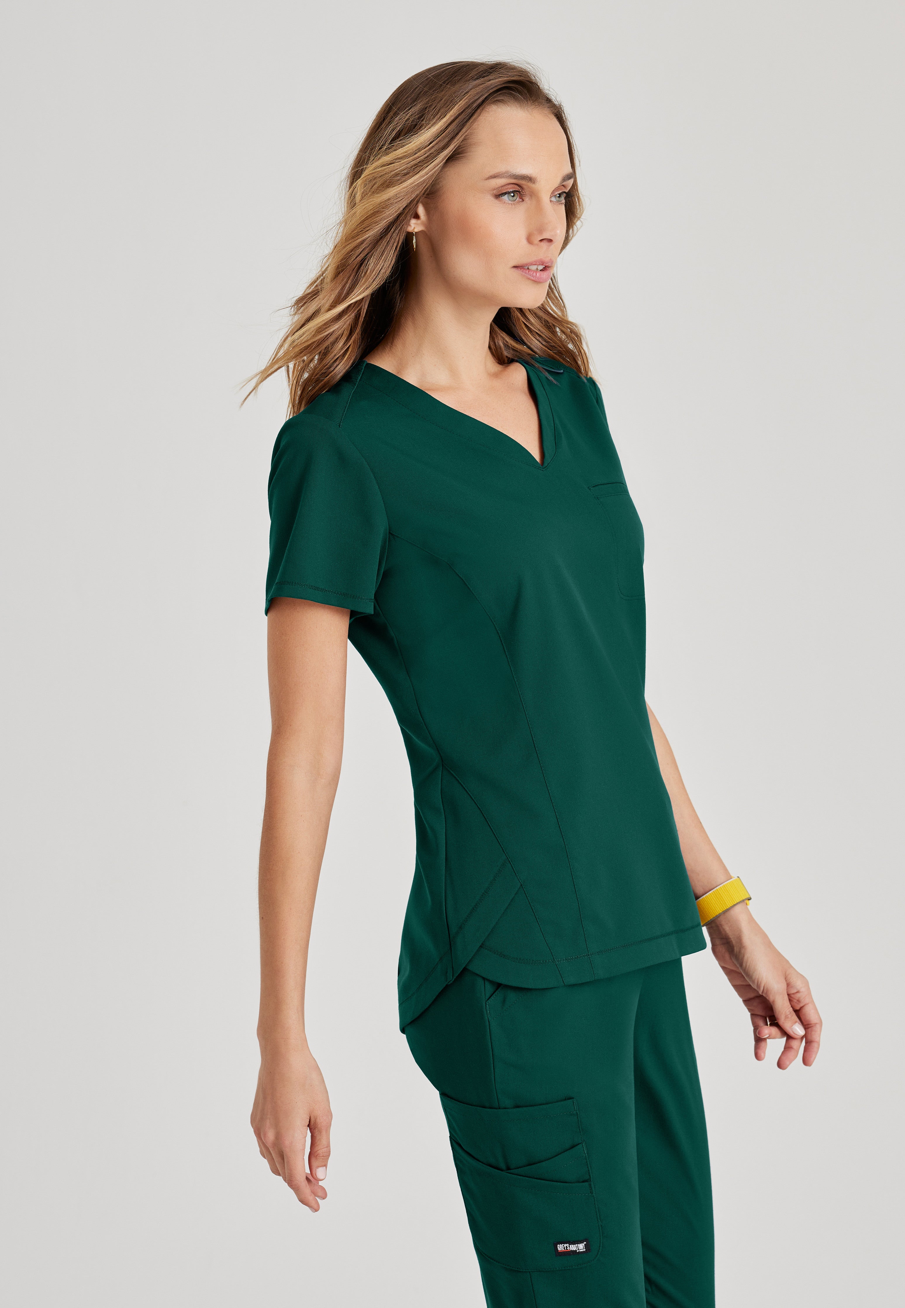 Side View of the Capri 2-Pocket Hourglass V-Neck Scrub Top in Hunter Green from Grey's Anatomy™ by Barco Spandex Stretch