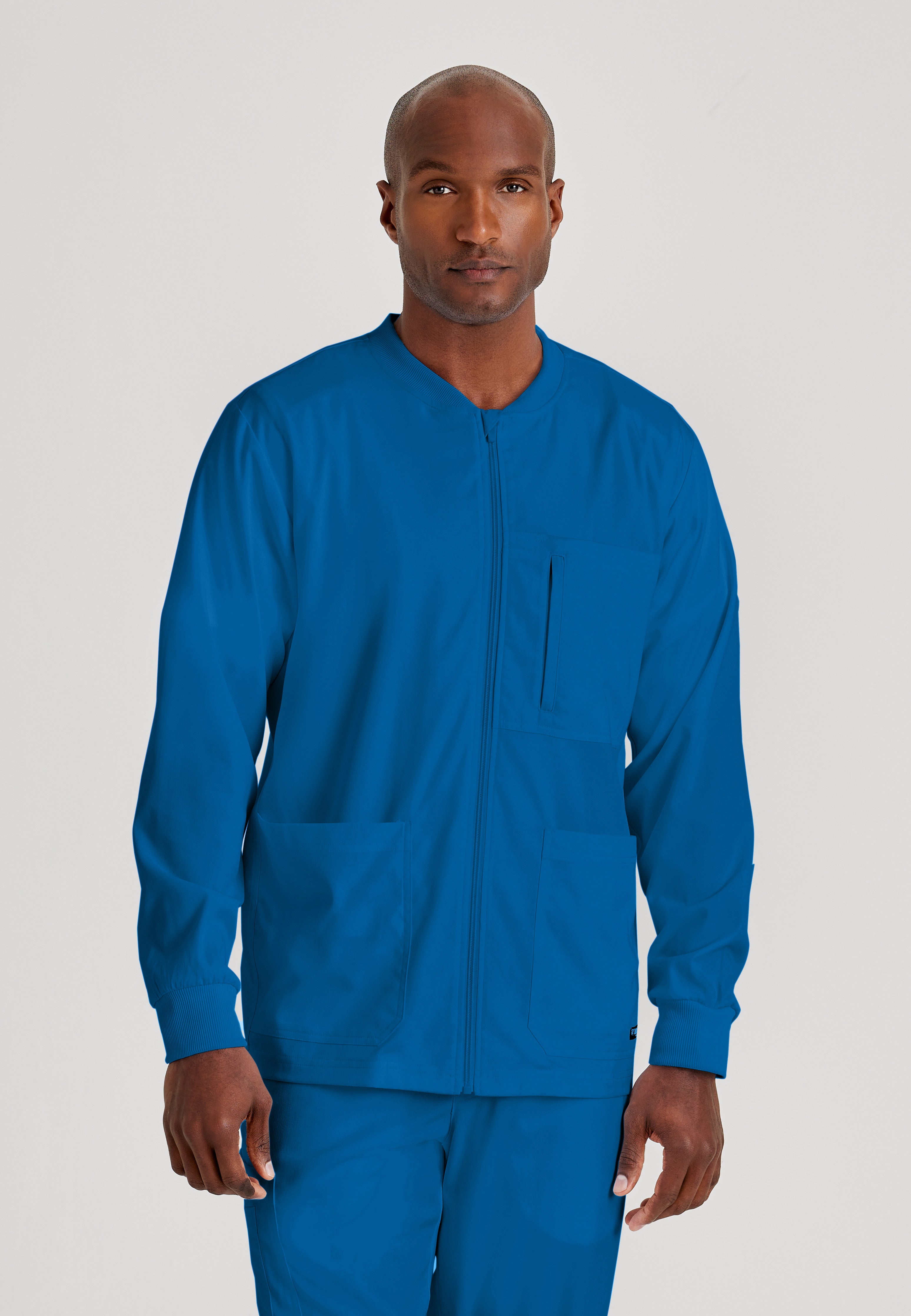 Front View of the React 5-Pocket Crewneck Warmup Scrub Jacket in New Royal from Grey's Anatomy™ by Barco Spandex Stretch