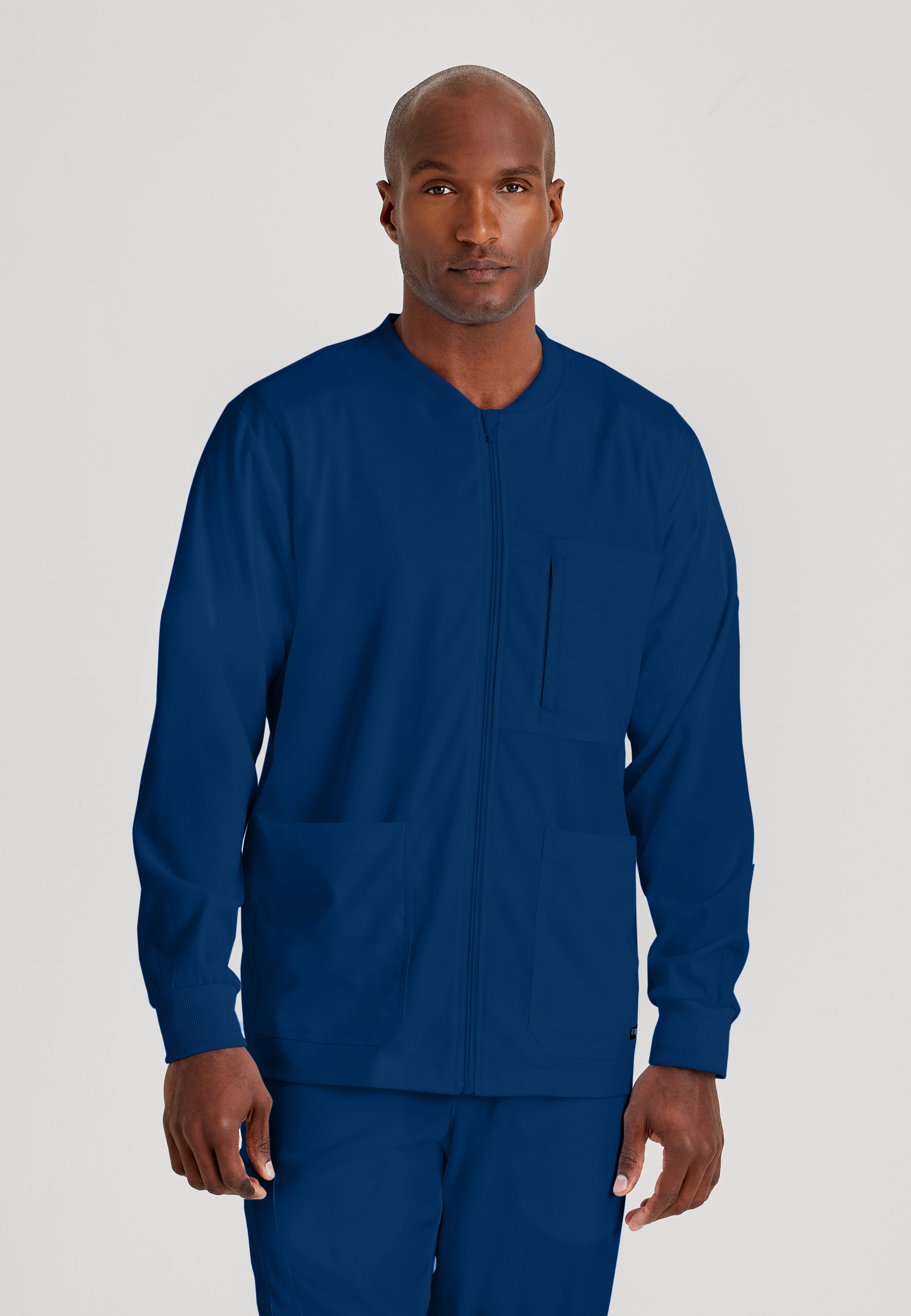 Front View of the React 5-Pocket Crewneck Warmup Scrub Jacket in Indigo from Grey's Anatomy™ by Barco Spandex Stretch