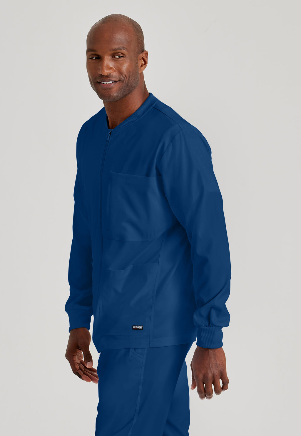 Side View of the React 5-Pocket Crewneck Warmup Scrub Jacket in Indigo from Grey's Anatomy™ by Barco Spandex Stretch