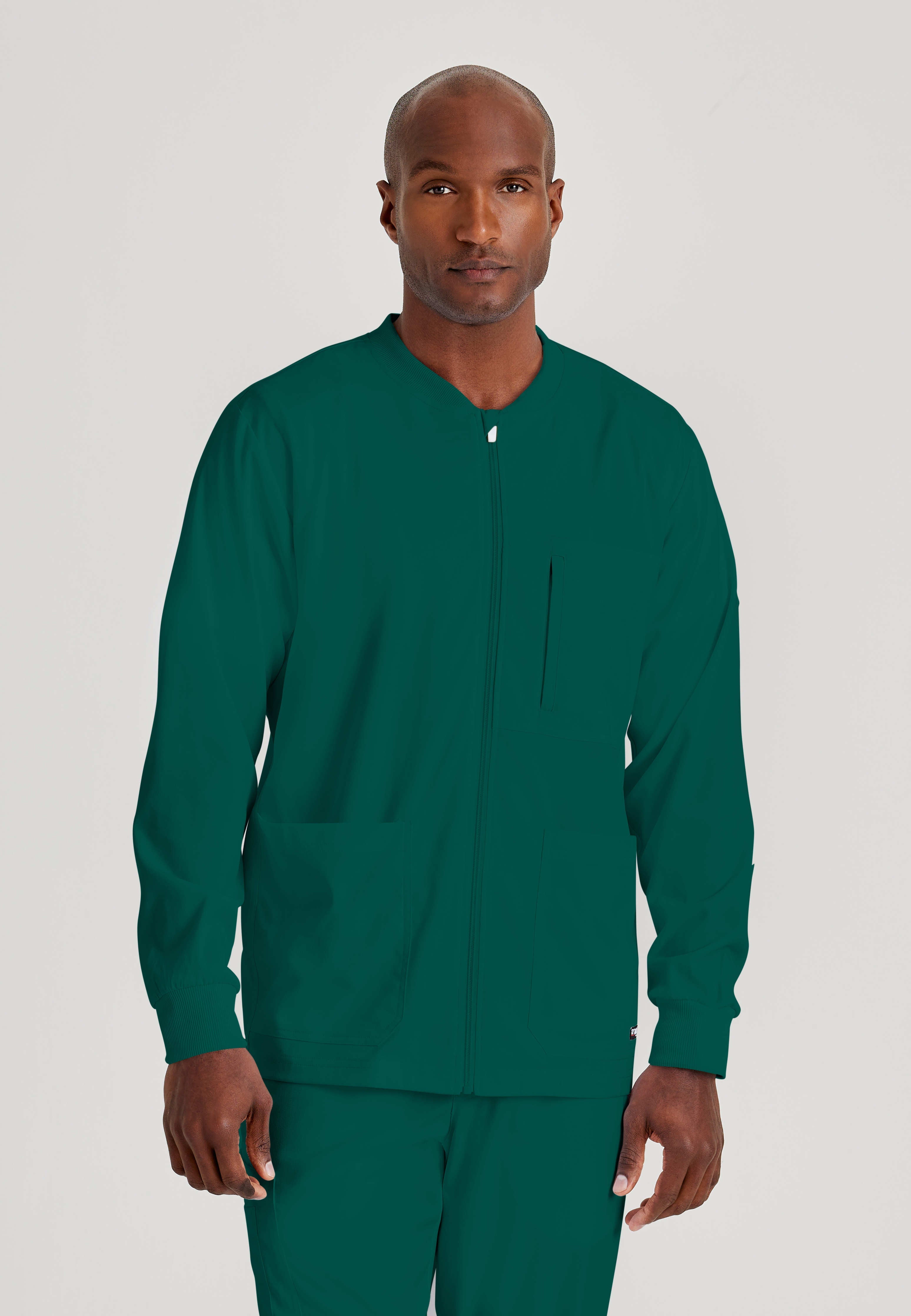 Front View of the React 5-Pocket Crewneck Warmup Scrub Jacket in Hunter Green from Grey's Anatomy™ by Barco Spandex Stretch
