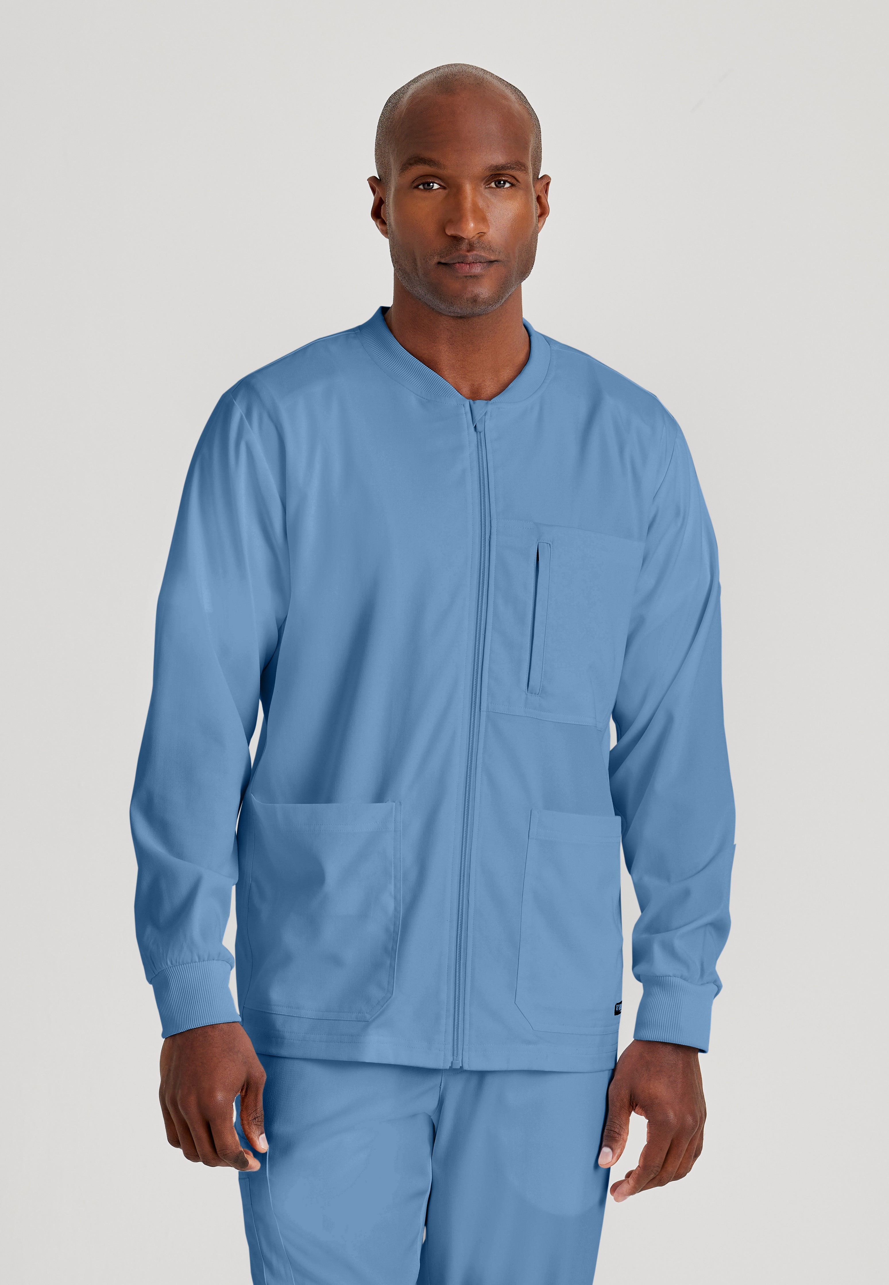 Front View of the React 5-Pocket Crewneck Warmup Scrub Jacket in Ciel Blue from Grey's Anatomy™ by Barco Spandex Stretch