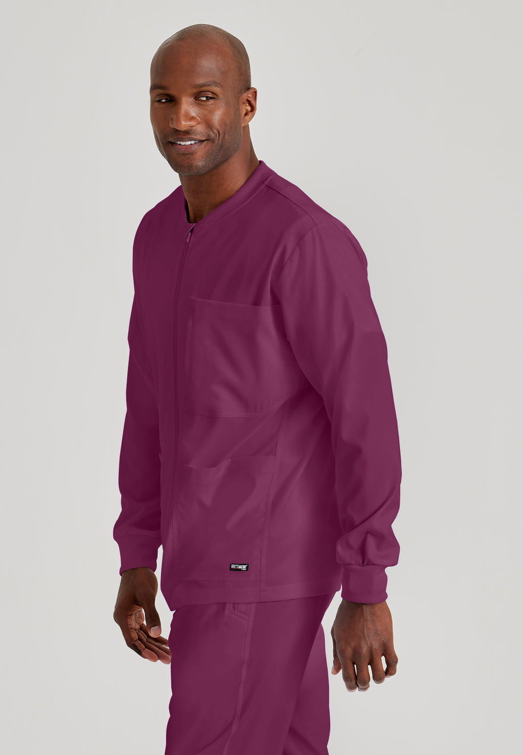 Side View of the React 5-Pocket Crewneck Warmup Scrub Jacket in Wine from Grey's Anatomy™ by Barco Spandex Stretch