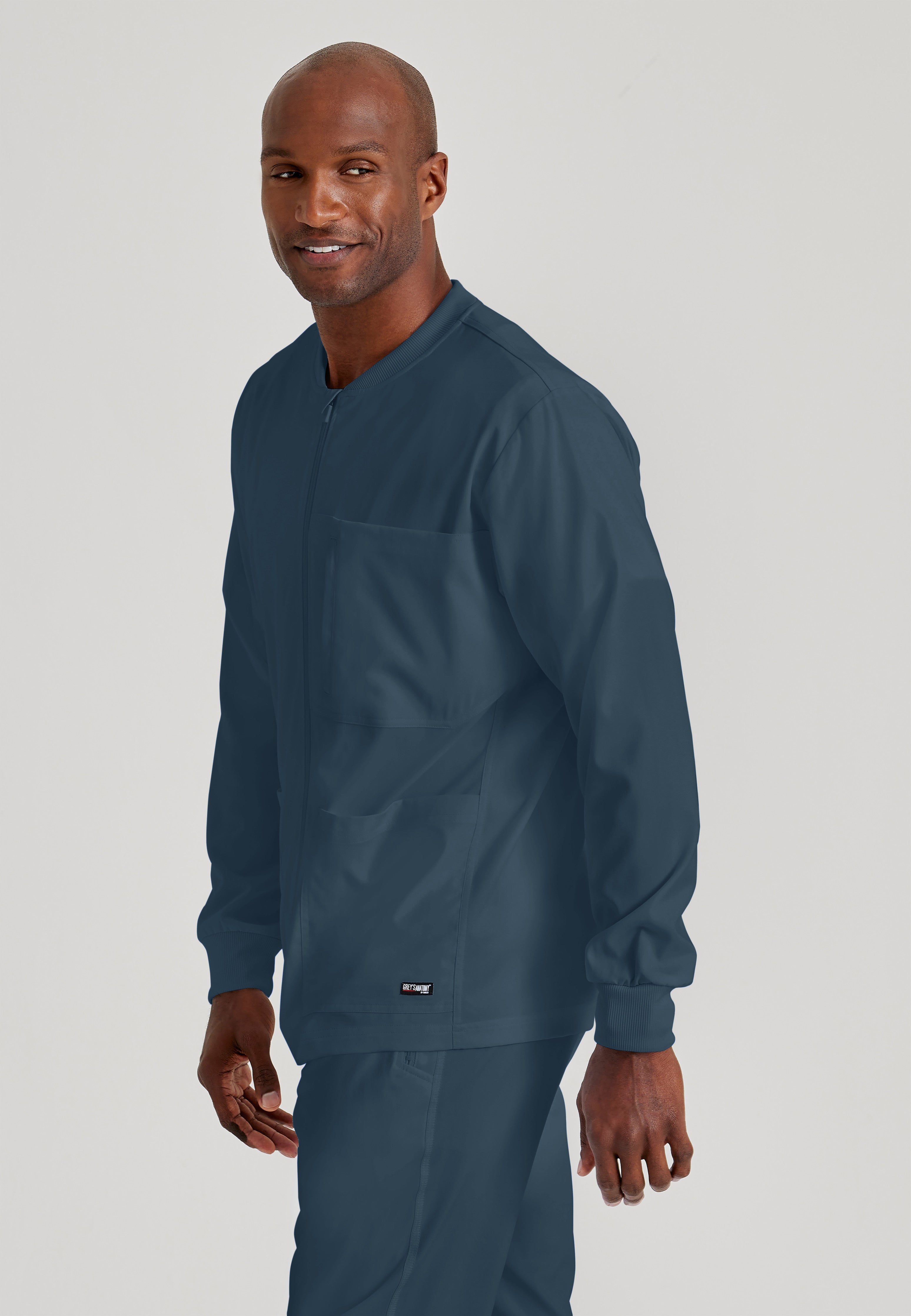 Side View of the React 5-Pocket Crewneck Warmup Scrub Jacket in Steel from Grey's Anatomy™ by Barco Spandex Stretch