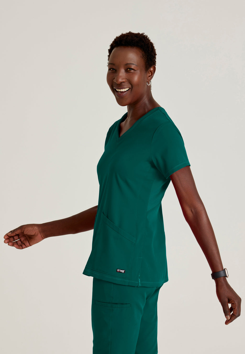 Side View of the Serena 3-Pocket Curved V-Neck Scrub Top in Hunter Green from Grey's Anatomy™ by Barco Spandex Stretch