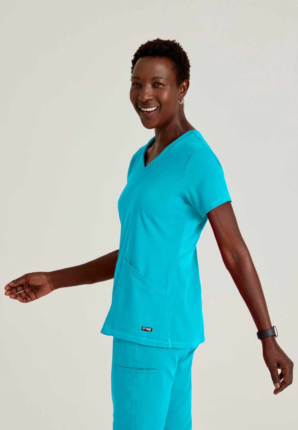 Side View of the Serena 3-Pocket Curved V-Neck Scrub Top in Teal from Grey's Anatomy™ by Barco Spandex Stretch