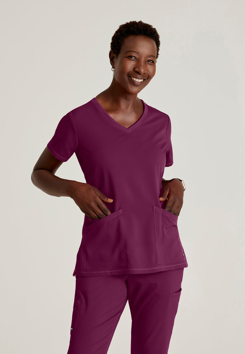 Front View of the Serena 3-Pocket Curved V-Neck Scrub Top in Wine from Grey's Anatomy™ by Barco Spandex Stretch