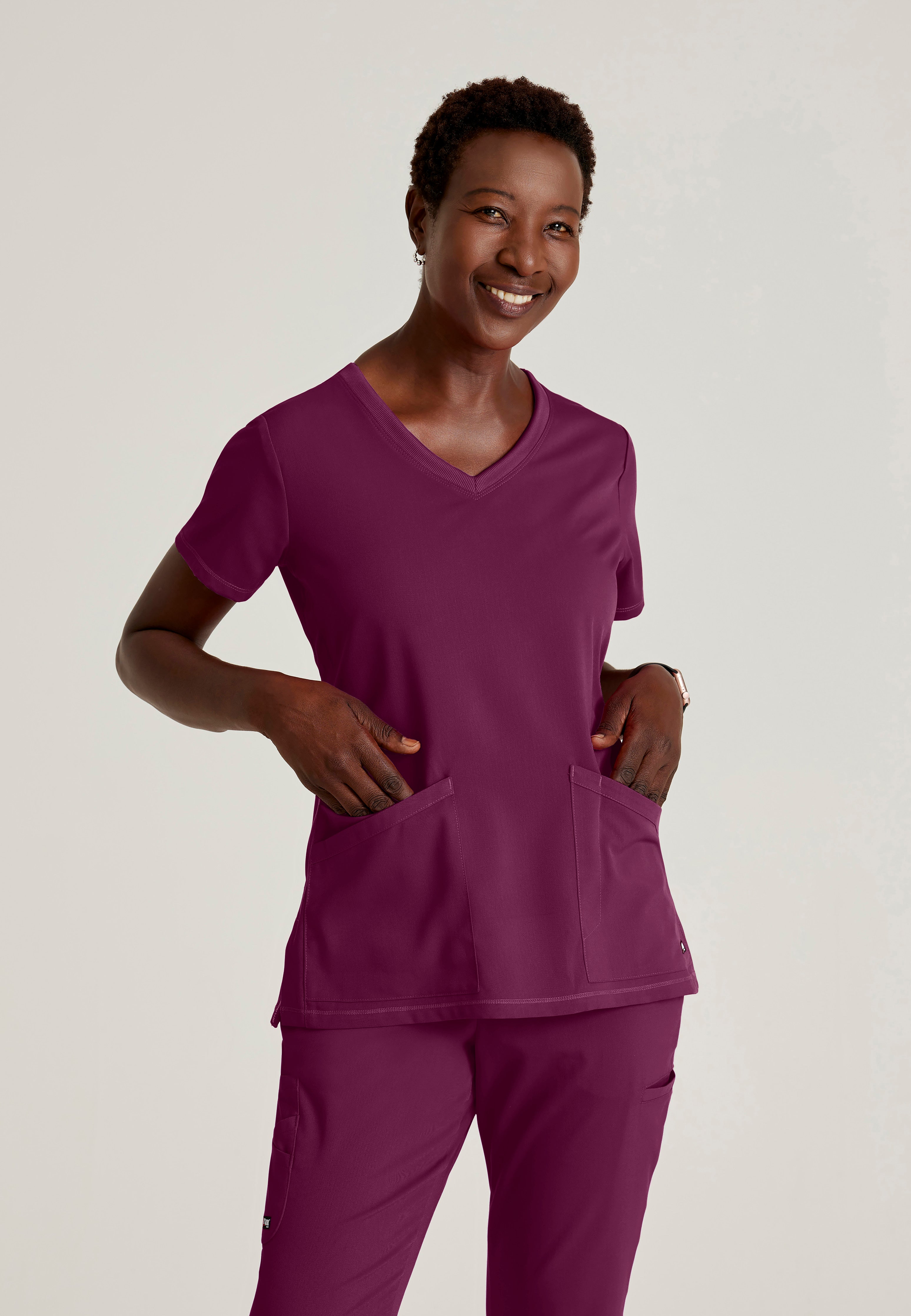 Front View of the Serena 3-Pocket Curved V-Neck Scrub Top in Wine from Grey's Anatomy™ by Barco Spandex Stretch