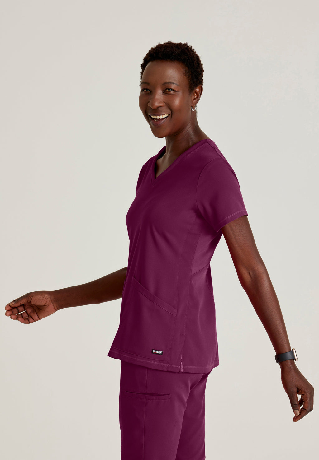 Side View of the Serena 3-Pocket Curved V-Neck Scrub Top in Wine from Grey's Anatomy™ by Barco Spandex Stretch