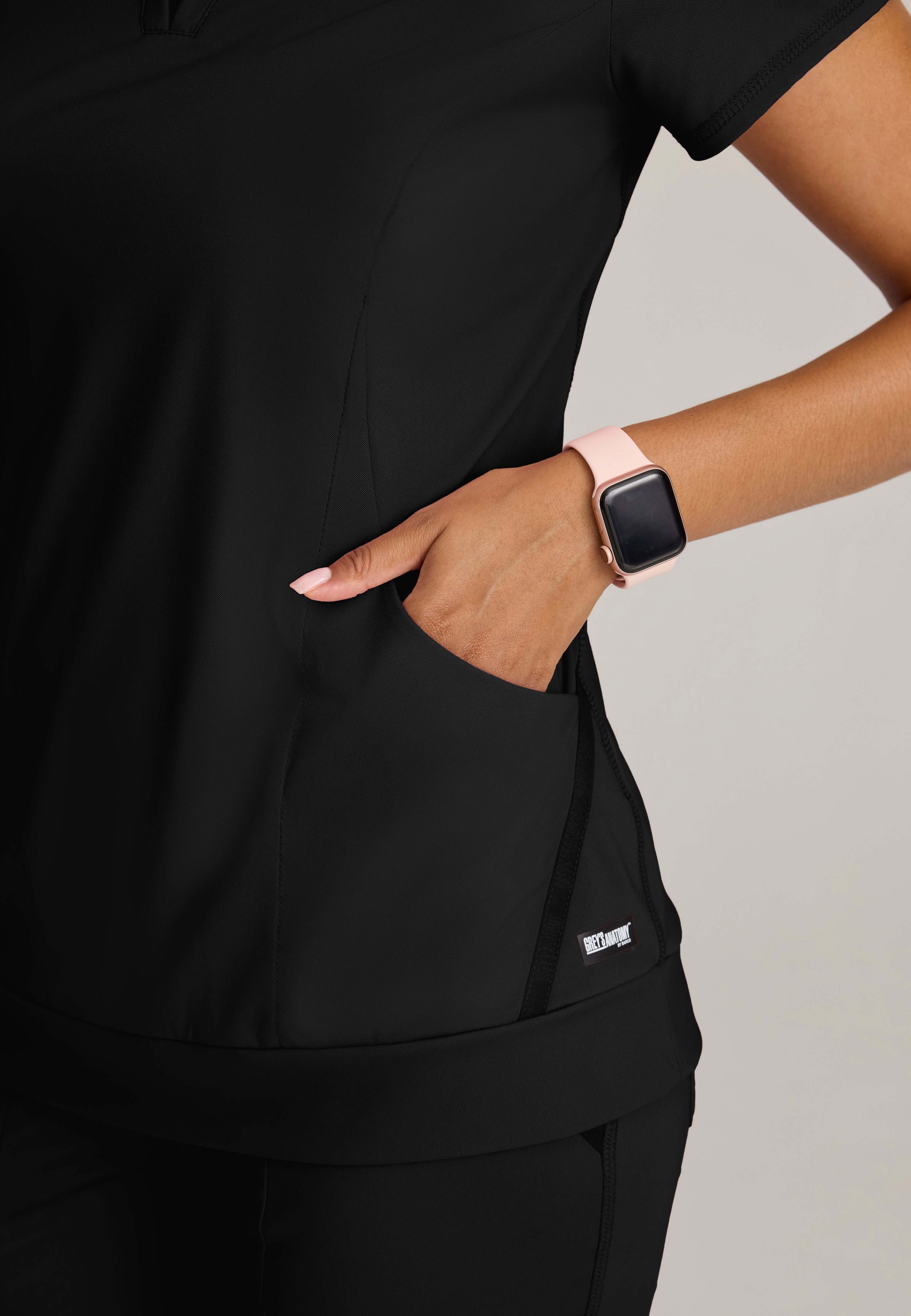 Detail Shot of the Motivate Curved V-Neck Knit Scrub Top in Black from Grey's Anatomy™ by Barco Knit Stretch