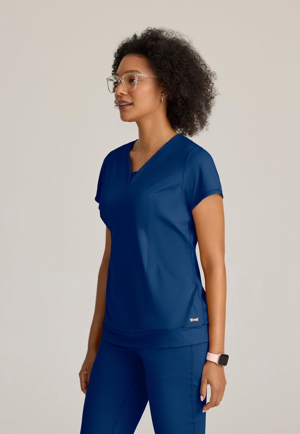 Side View of the Motivate Curved V-Neck Knit Scrub Top in Indigo from Grey's Anatomy™ by Barco Knit Stretch
