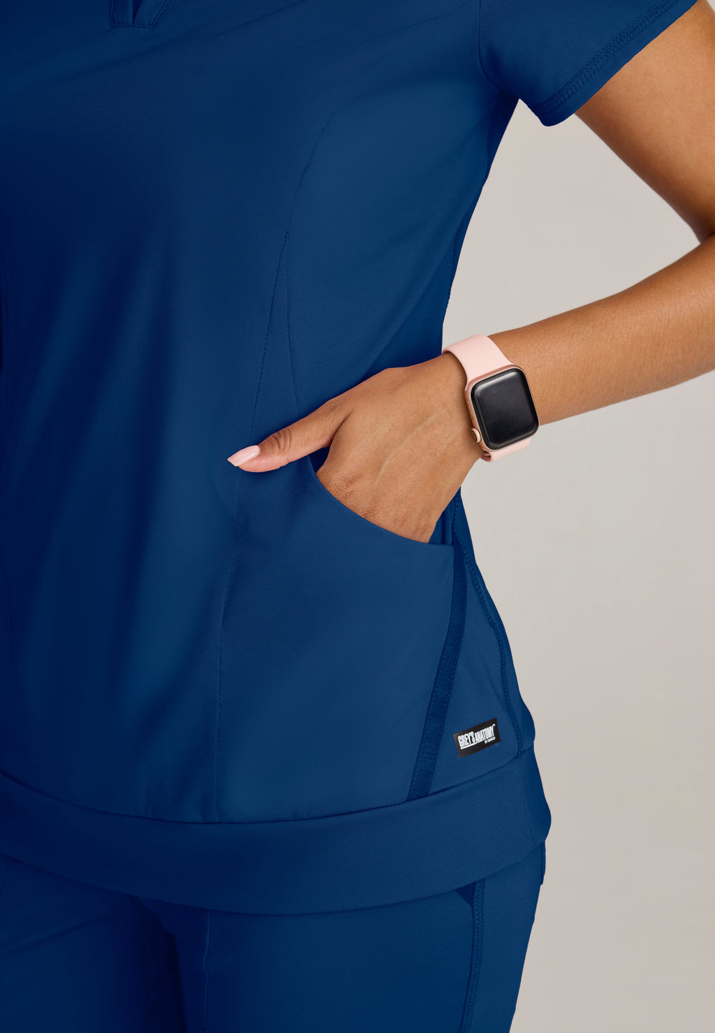 Detail Shot of the Motivate Curved V-Neck Knit Scrub Top in Indigo from Grey's Anatomy™ by Barco Knit Stretch