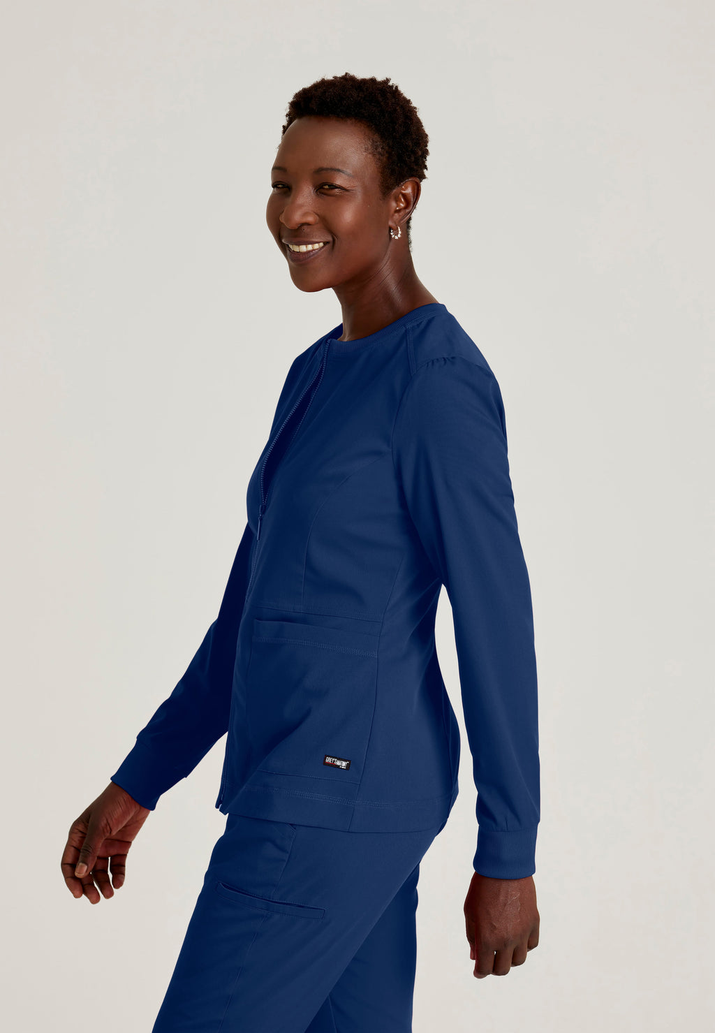Side View of the Millie 3-Pocket Crewneck Scrub Jacket in Indigo from Grey's Anatomy™ by Barco Spandex Stretch