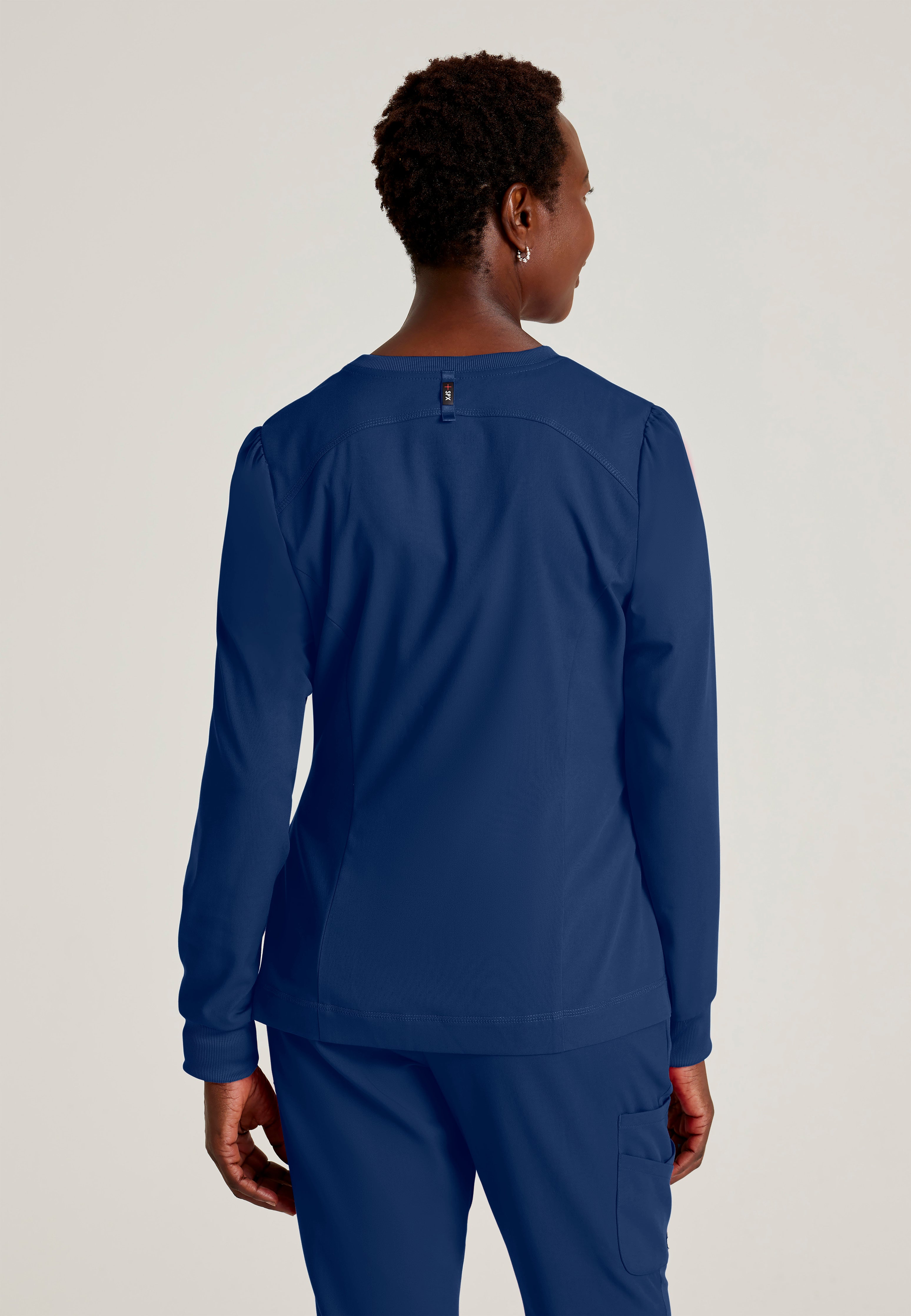 Back View of the Millie 3-Pocket Crewneck Scrub Jacket in Indigo from Grey's Anatomy™ by Barco Spandex Stretch
